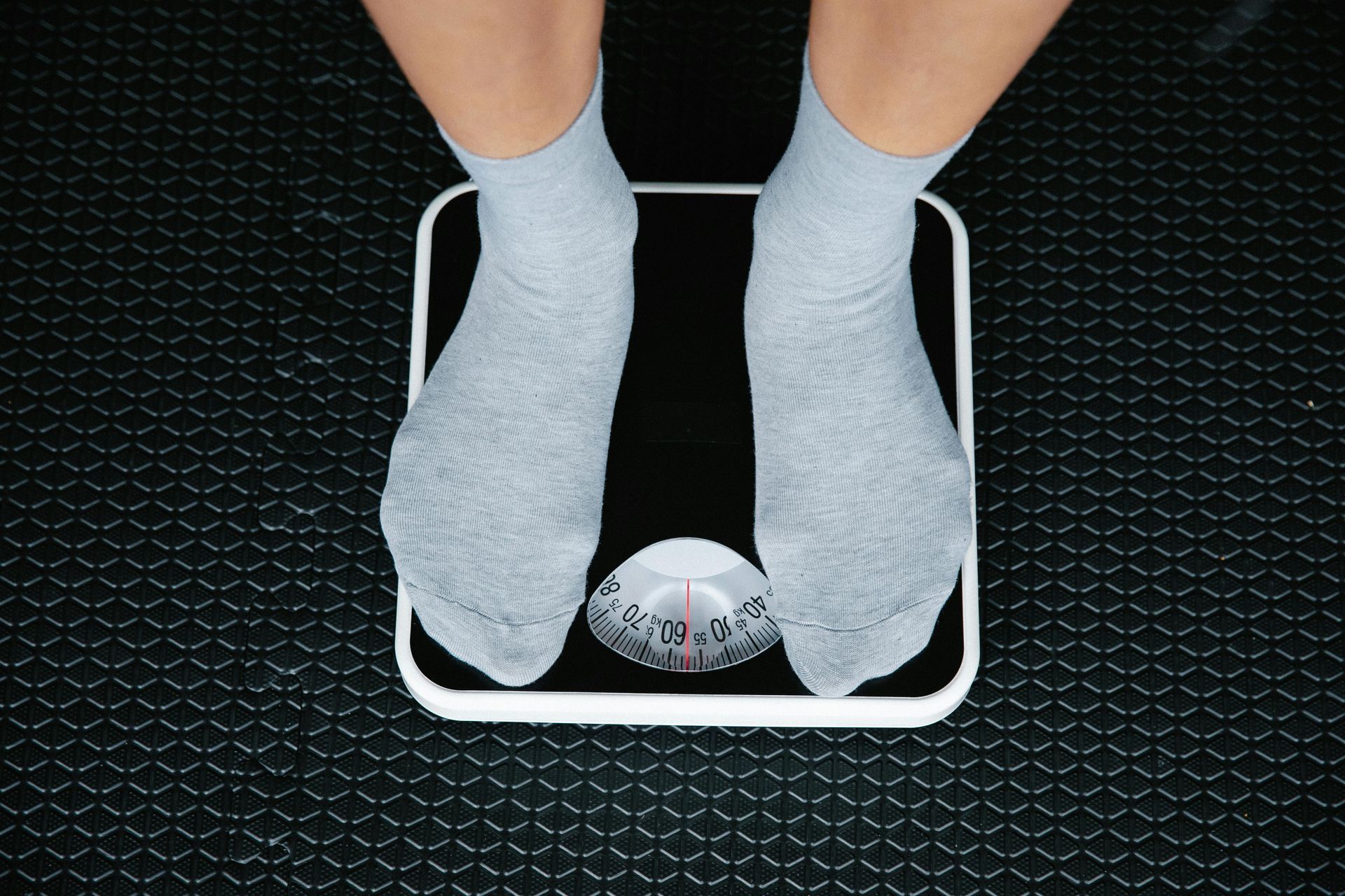 Person's feet in grey socks standing on a black and white scale on a textured black surface.