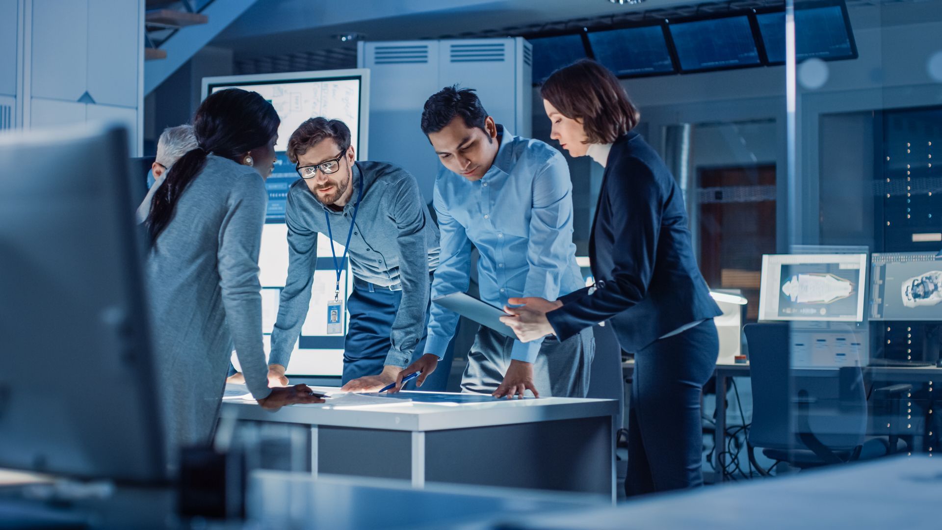 People deliberating at a conference room table in a high-tech office setting.