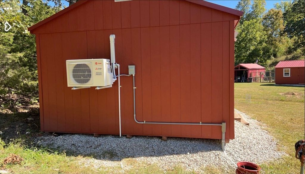 Red shed with an air conditioner unit mounted on the side. Electrical conduit runs along the wall.