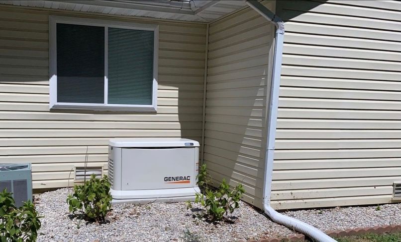 White generator next to a house with beige siding, window, and gravel.