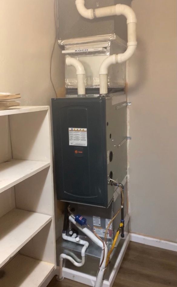 A Rheem furnace with white PVC pipes in a corner next to a white shelf.