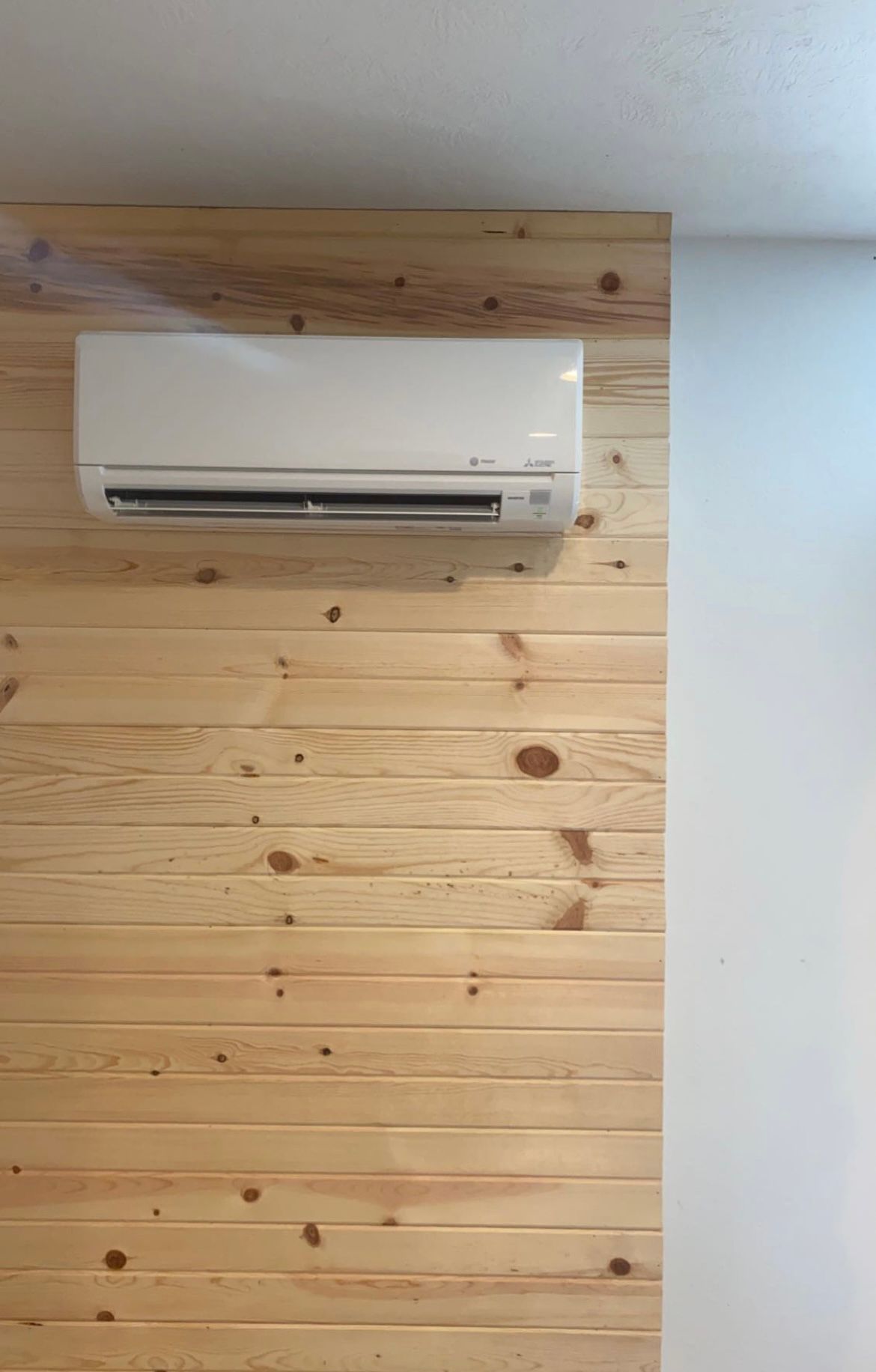 Wall-mounted air conditioner on a wood plank wall, next to a white wall.