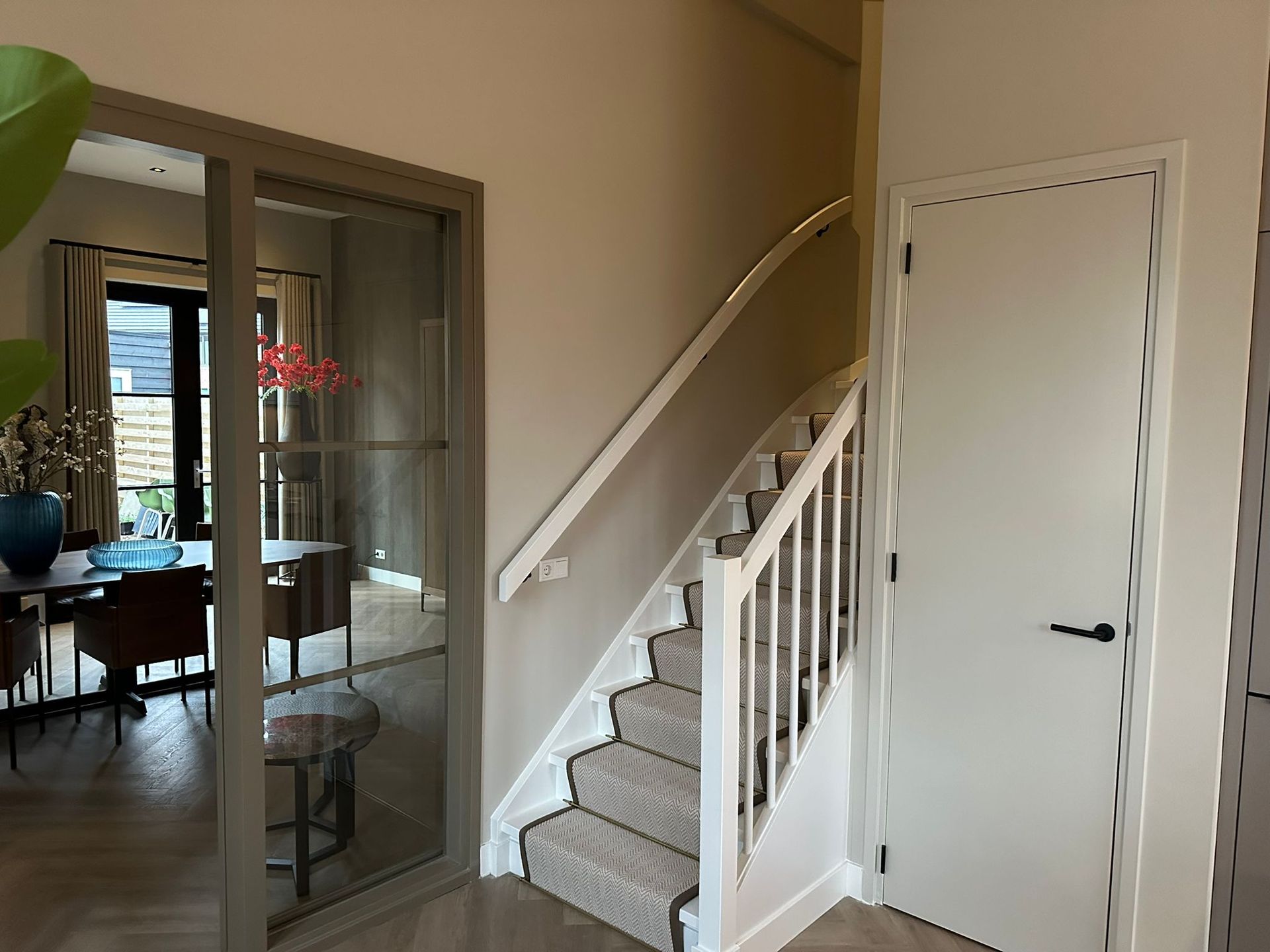 Een lichte binnenhal met een met tapijt beklede trap met witte leuningen, een witte deur en een kamerscherm van glas.