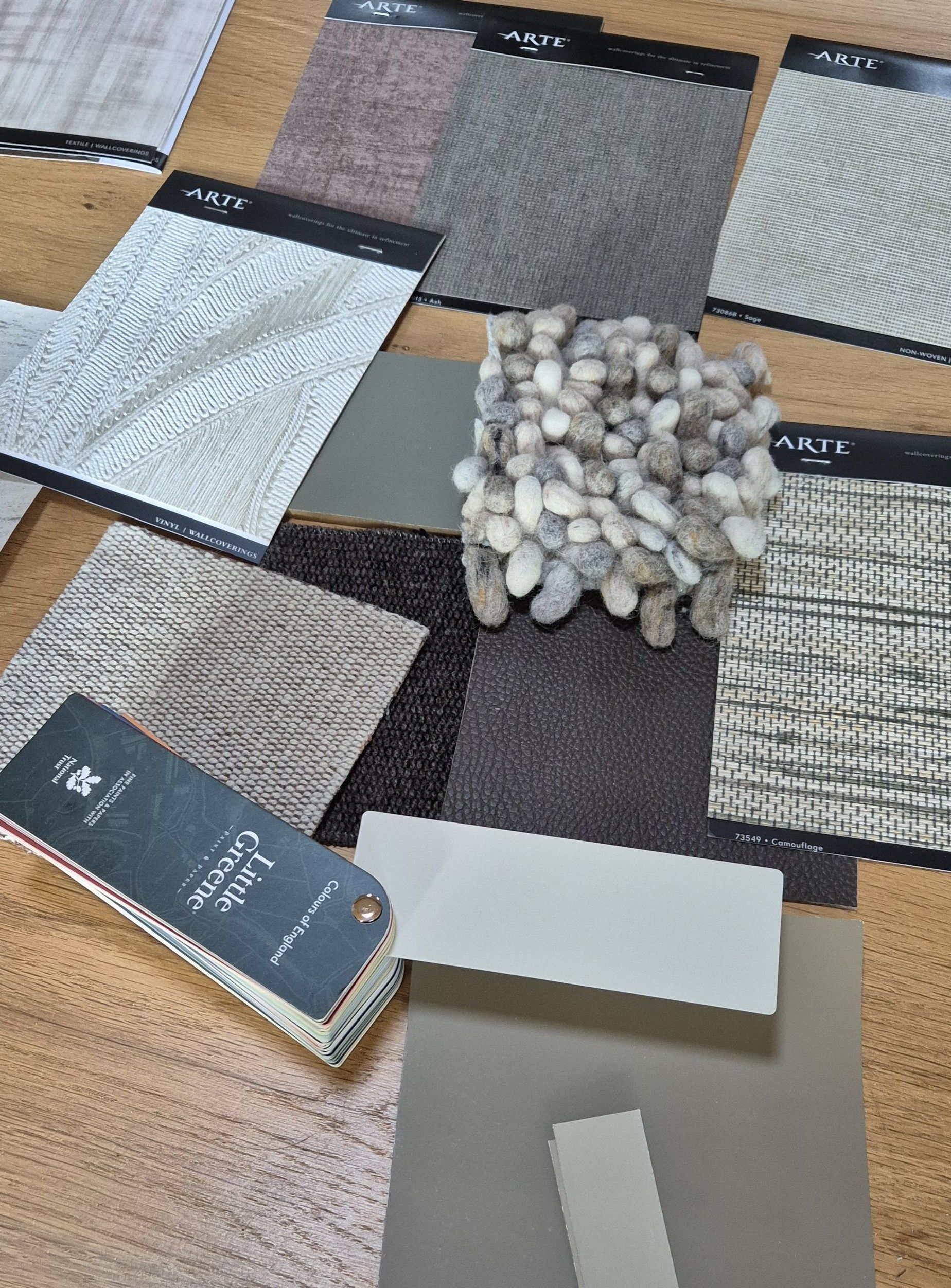 Diverse stalen van stof en steen in neutrale grijs-, bruin- en beigetinten, uitgestald op een houten ondergrond.