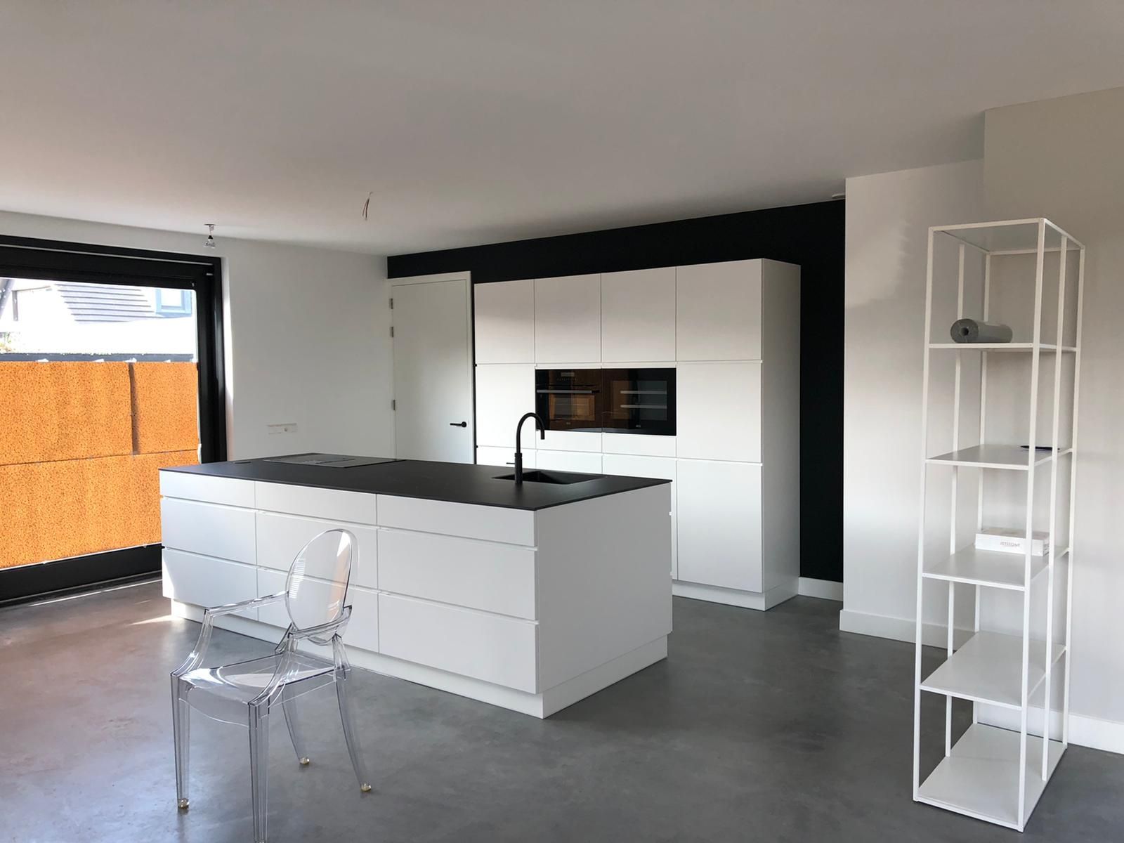 Moderne keuken met een wit kookeiland, bijpassende keukenkastjes, een transparante stoel en een wit metalen rek.