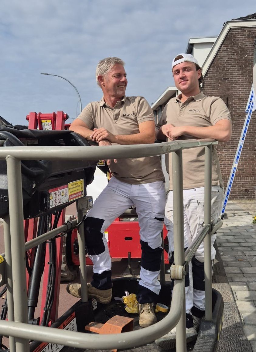 Een werknemer in een werkbroek en een T-shirt plakt tape op een witte muur in een gang naast een trappenhuis.