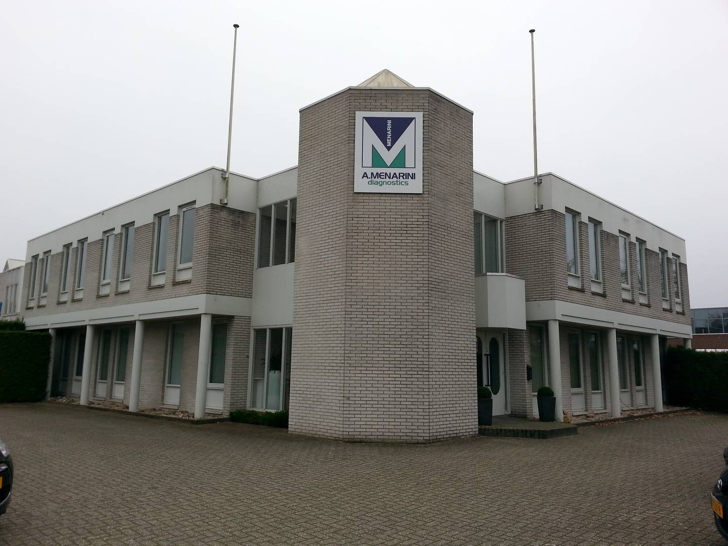 Een commercieel gebouw van twee verdiepingen met een centrale, hoge bakstenen toegangstoren met een blauw M-logo.