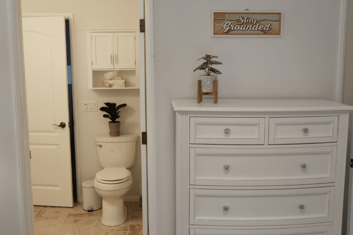 A bathroom with a toilet , dresser and a sign on the wall.