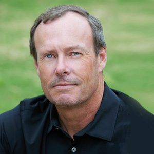 Cannon Kristofferson in a black shirt is sitting in the grass and looking at the camera.