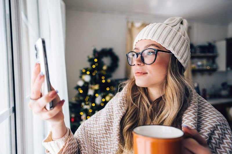 A woman is taking a selfie with her cell phone while holding a cup of coffee.