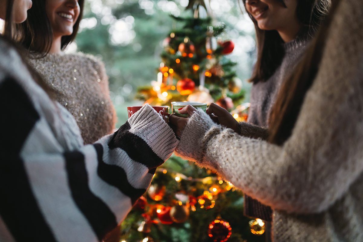 A group of women are holding hands in front of a christmas tree.