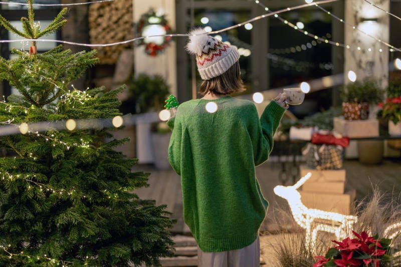 A woman in a green sweater is standing in front of a christmas tree.