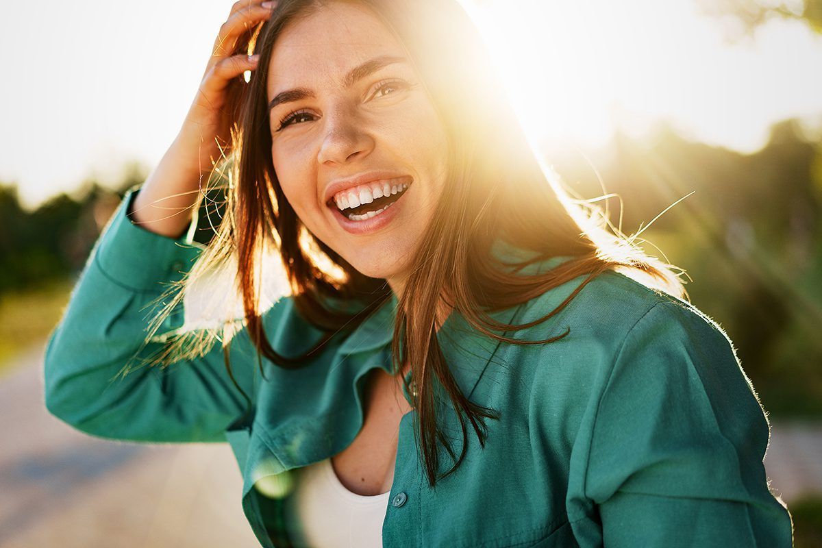 A woman in a green shirt is smiling with the sun shining on her face.