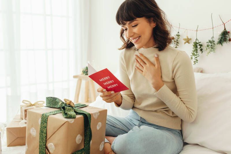 A woman is sitting on a couch reading a christmas card.