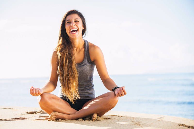 A woman is sitting in a lotus position on the beach.