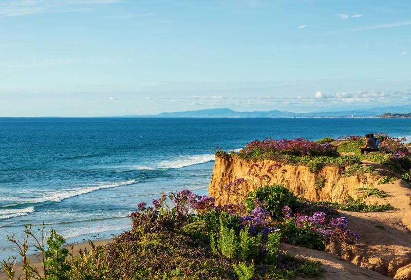 A person is sitting on a cliff overlooking the ocean.