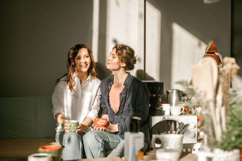 Two women are sitting on a couch drinking coffee.