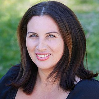 A woman with long dark hair is smiling and wearing a black shirt.