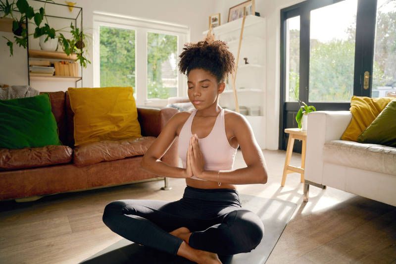 A woman is sitting on a yoga mat in a living room.