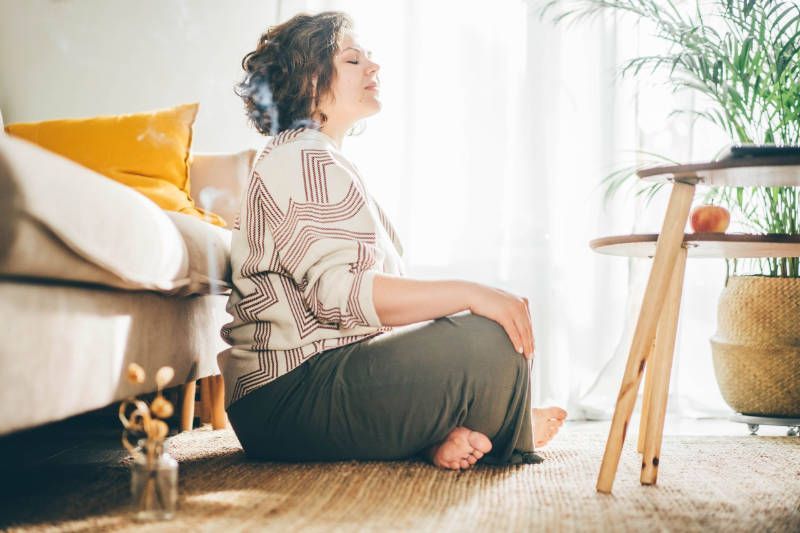 A woman is sitting on the floor in a living room with her eyes closed.