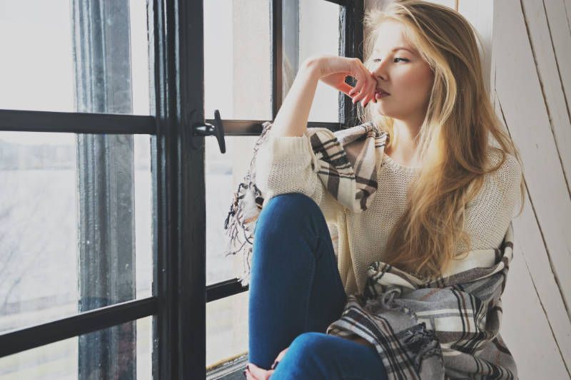 A woman is sitting on a window sill looking out the window.