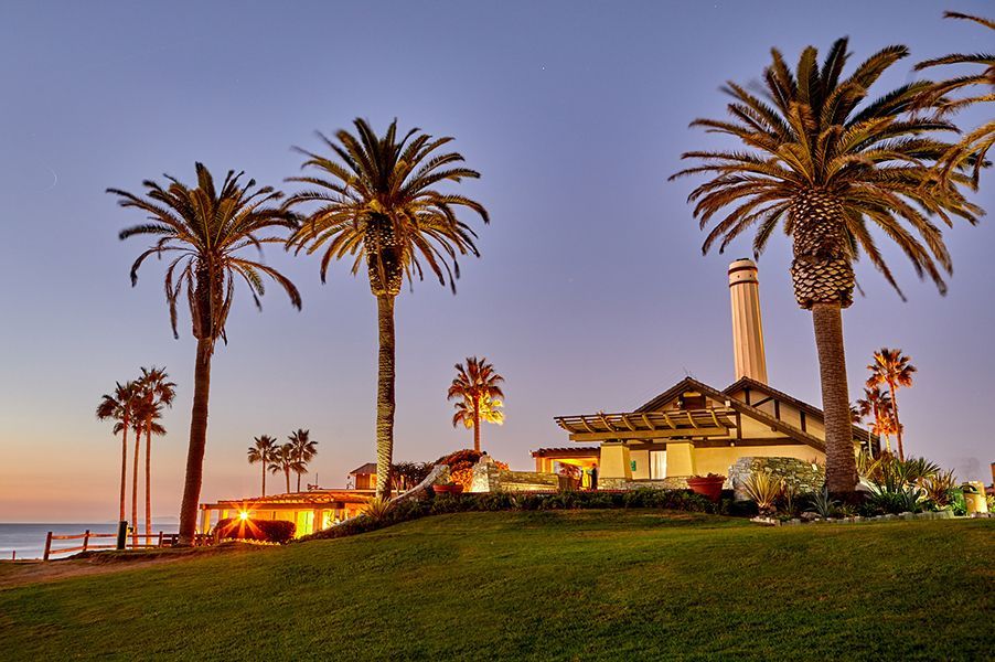 A house with palm trees and a lighthouse in the background