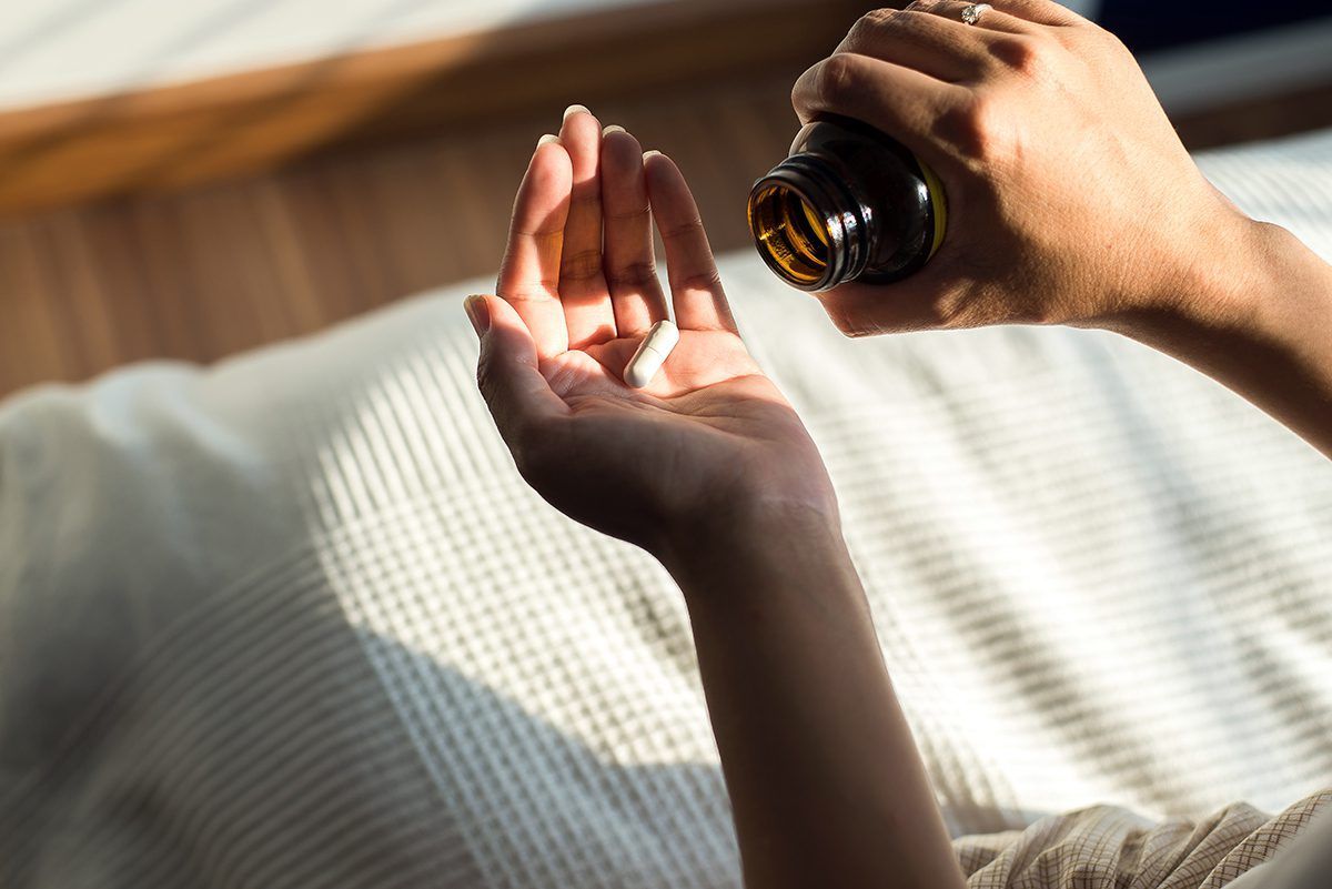 A person is taking a pill from a bottle in their hand.