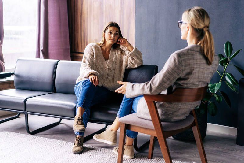 Two women are sitting on a couch talking to each other.