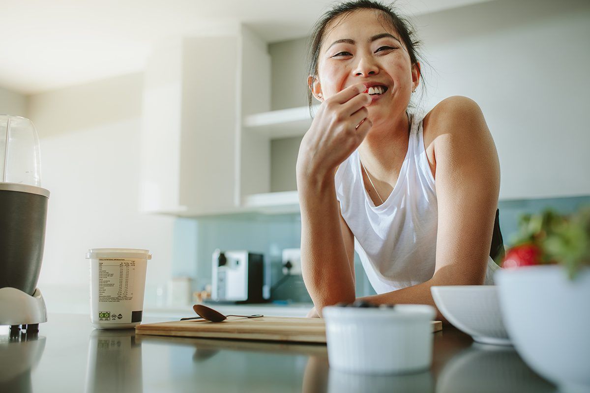 A woman is sitting at a kitchen counter eating food.