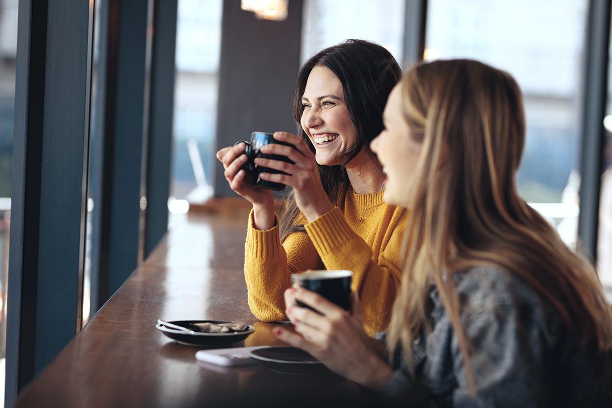 Two women are sitting at a table drinking coffee and laughing.