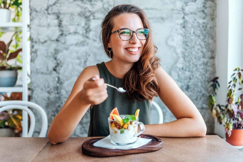 A woman is sitting at a table eating a fruit salad with a spoon.