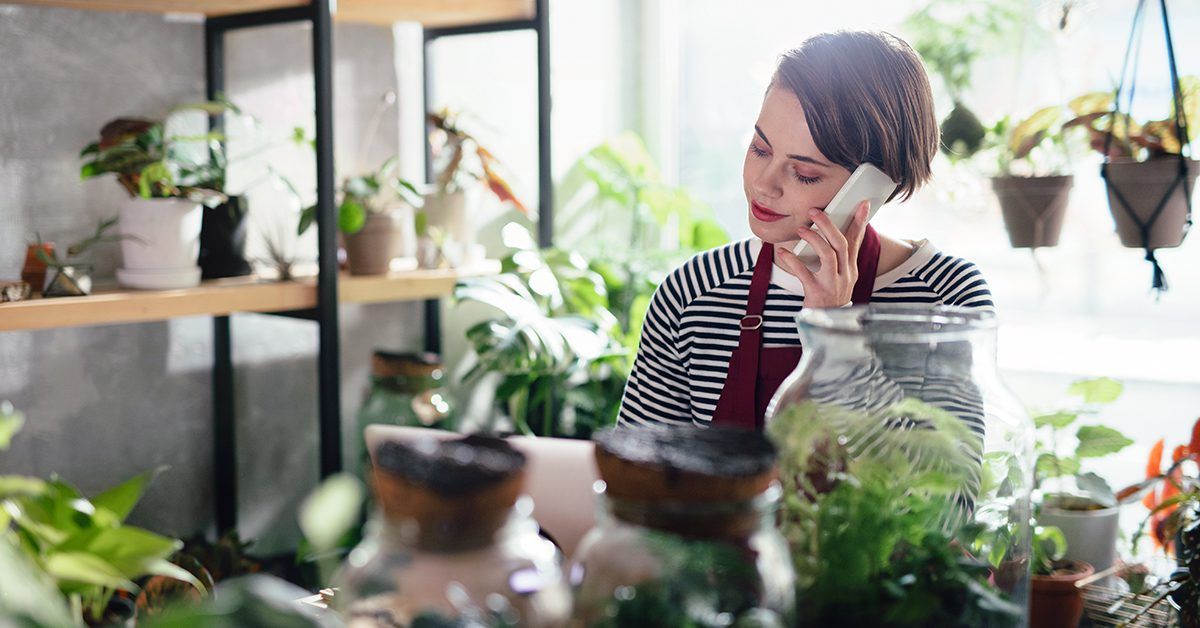 A woman is sitting at a table in a plant store talking on a cell phone.