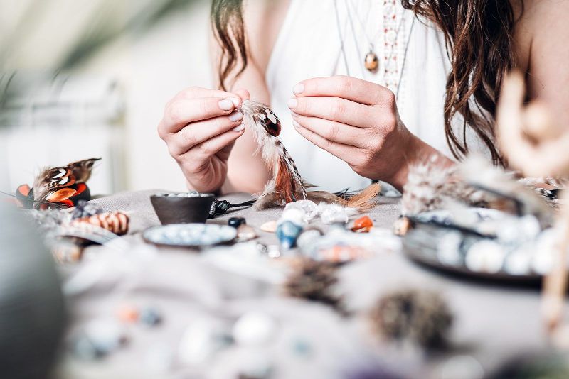 A woman is sitting at a table making a necklace with beads.