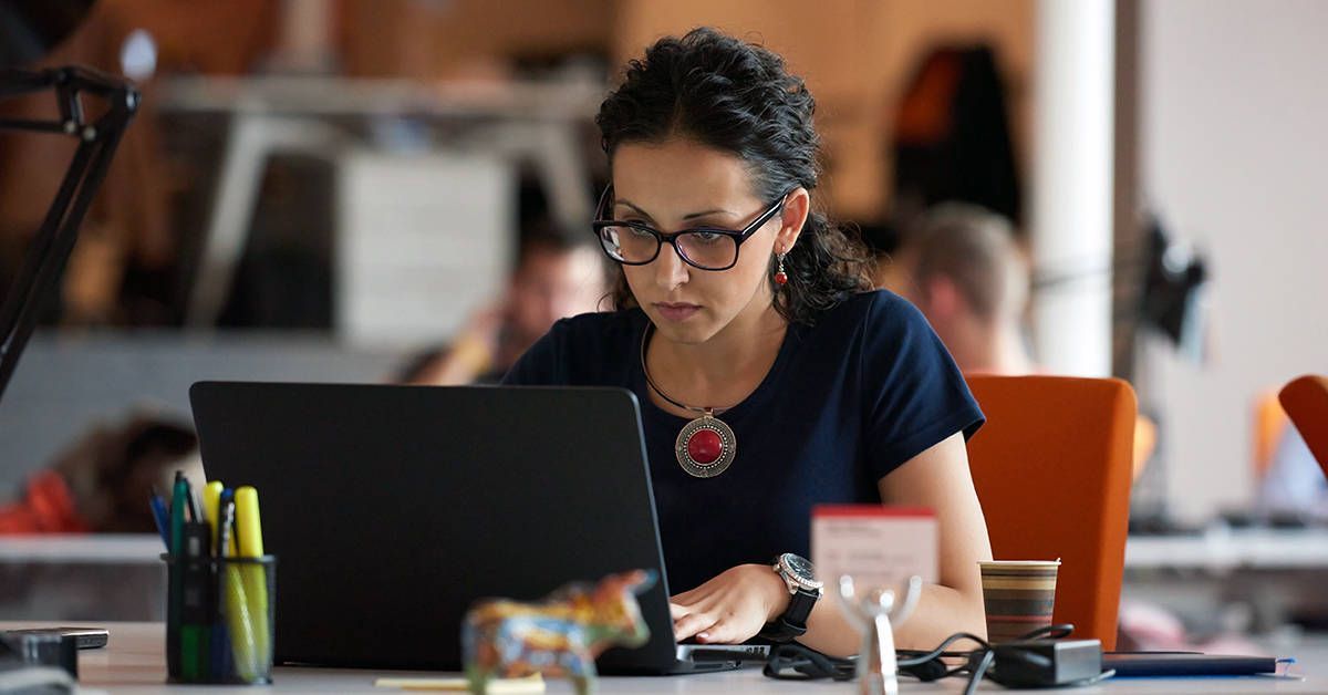 A woman is sitting at a desk using a laptop computer.