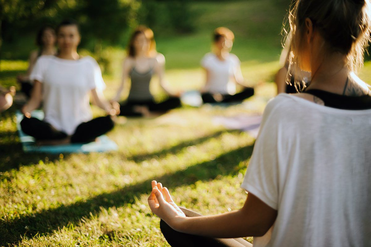 A group of people are sitting in a circle on yoga mats in a park.