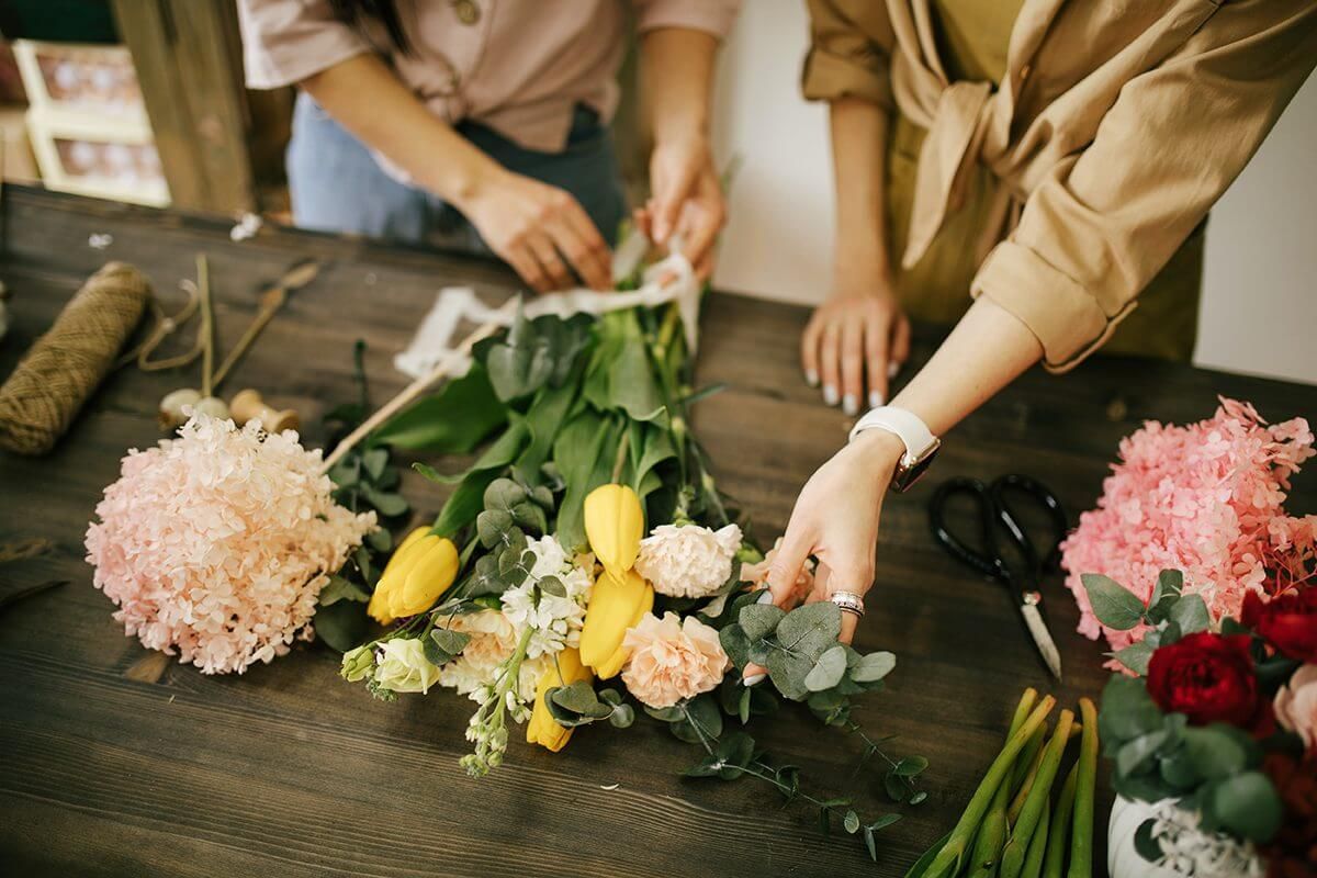 Two women are making a bouquet of flowers at a table.