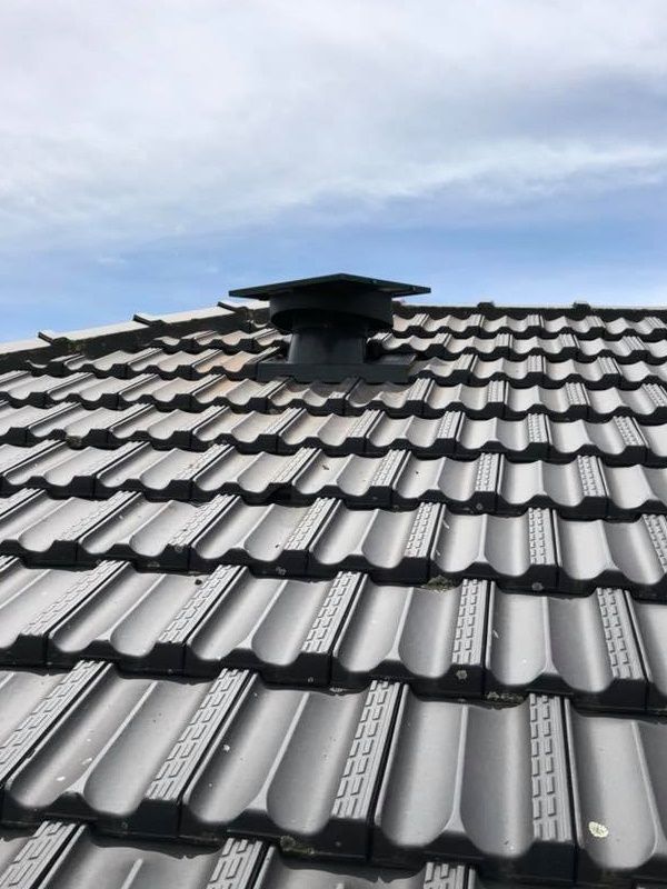 A Black Metal Roof With Dark Tiles and a Chimney Cap Against a Cloudy Sky — Gold Coast Skylights in Slacks Creek, QLD
