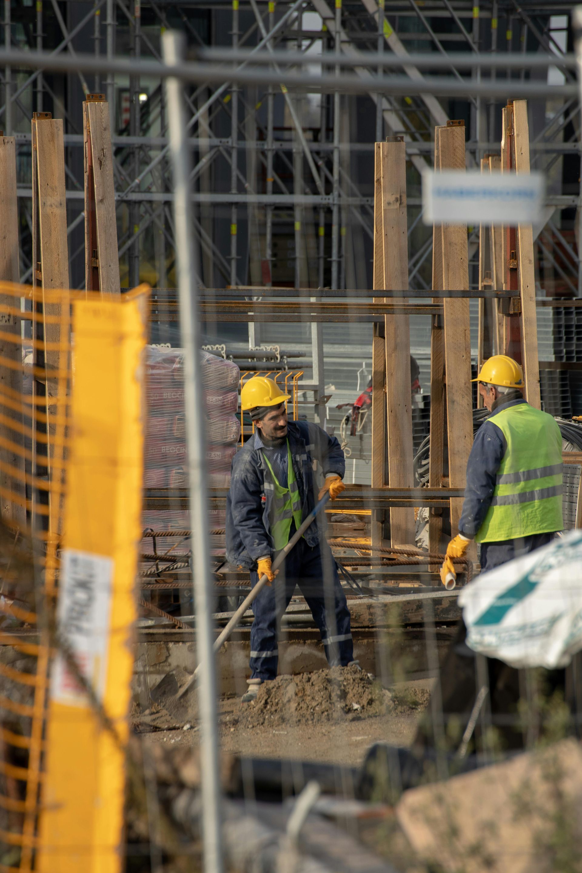 Two construction workers in yellow helmets working on a construction site.