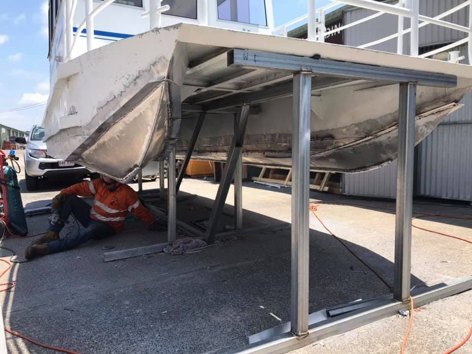 A Man is Laying on the Ground Next to a Boat — Jensen Welding & Fabrication in Chevallum, QLD