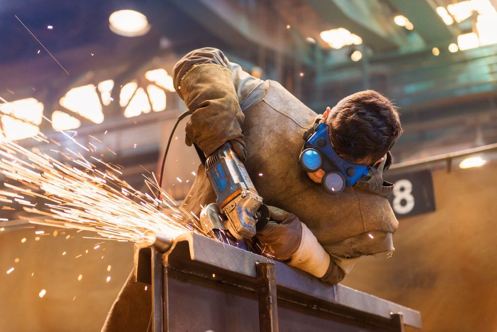 A Man is Grinding a Piece of Metal With a Grinder in a Factory — Jensen Welding & Fabrication in Chevallum, QLD