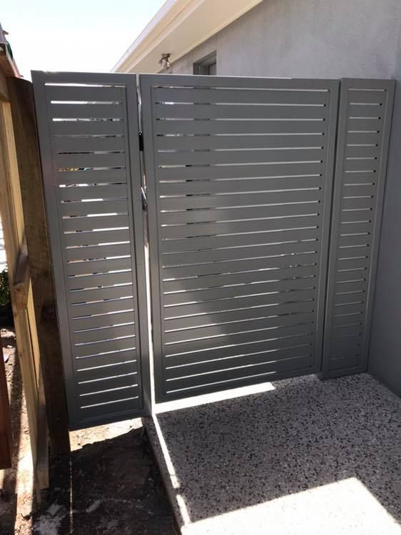 A Gray Fence With a Wooden Fence Behind It — Jensen Welding & Fabrication in Chevallum, QLD