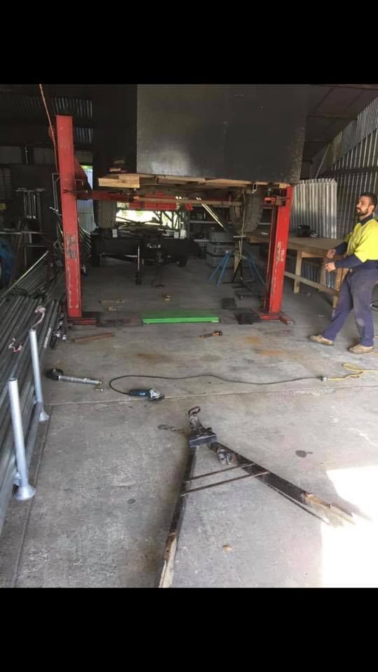 A Man is Standing in a Garage Next to a Lift — Jensen Welding & Fabrication in Chevallum, QLD