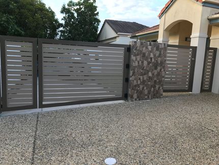 Modern gray metal driveway gate with stone pillar beside a house  — Jensen Welding & Fabrication in Chevallum, QLD