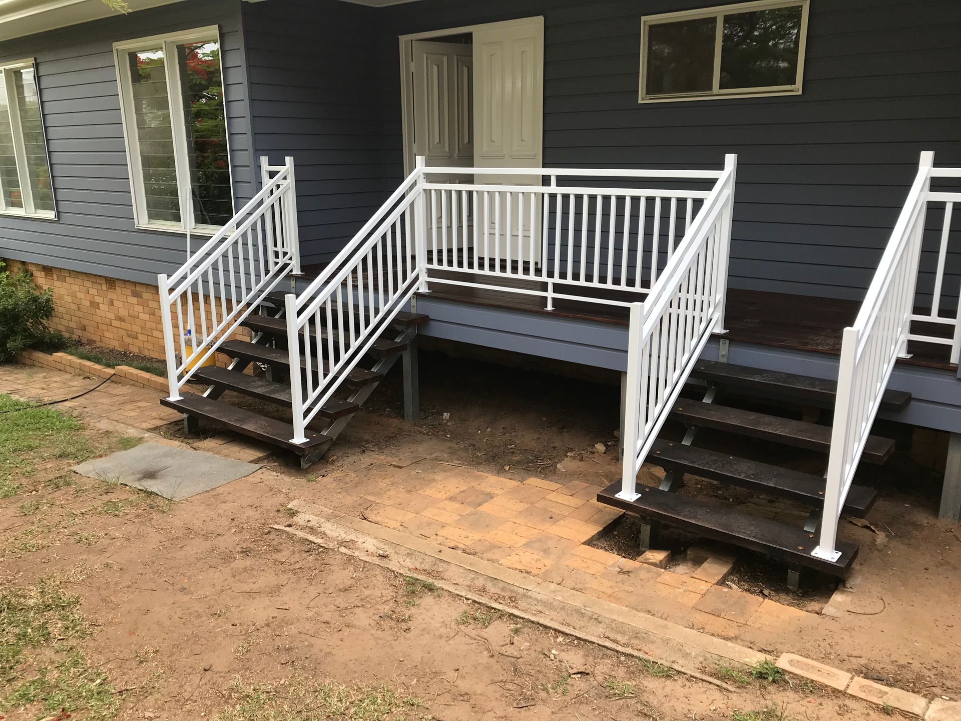 Front porch with white railings and dark steps on a gray house, with a small walkway and dirt yard.  — Jensen Welding & Fabrication in Chevallum, QLD