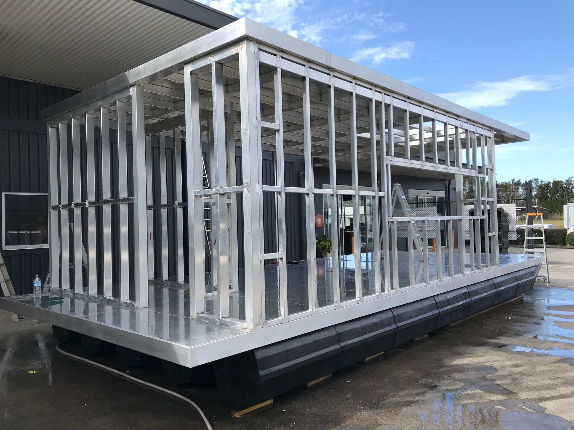 Metal-framed modular structure on a black floating platform beside a building, under construction — Jensen Welding & Fabrication in Chevallum, QLD