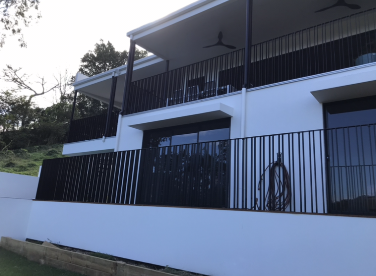 White two-story house with black railings and a sloped roof on a hillside — Jensen Welding & Fabrication in Chevallum, QLD