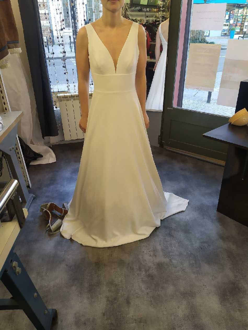 Une femme en robe de mariée blanche se tient dans une pièce.