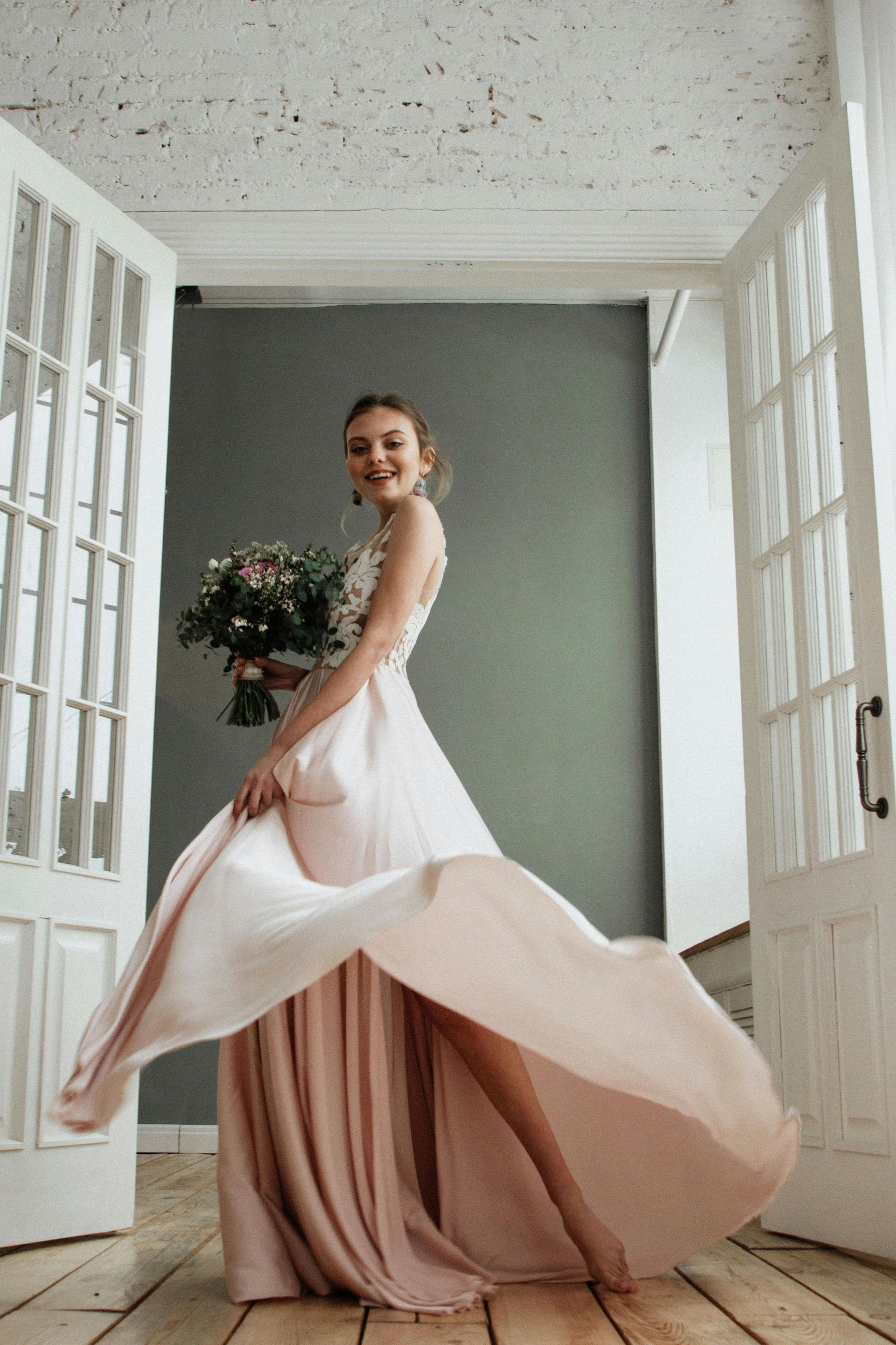 Une femme dans une longue robe rose tient un bouquet de fleurs.