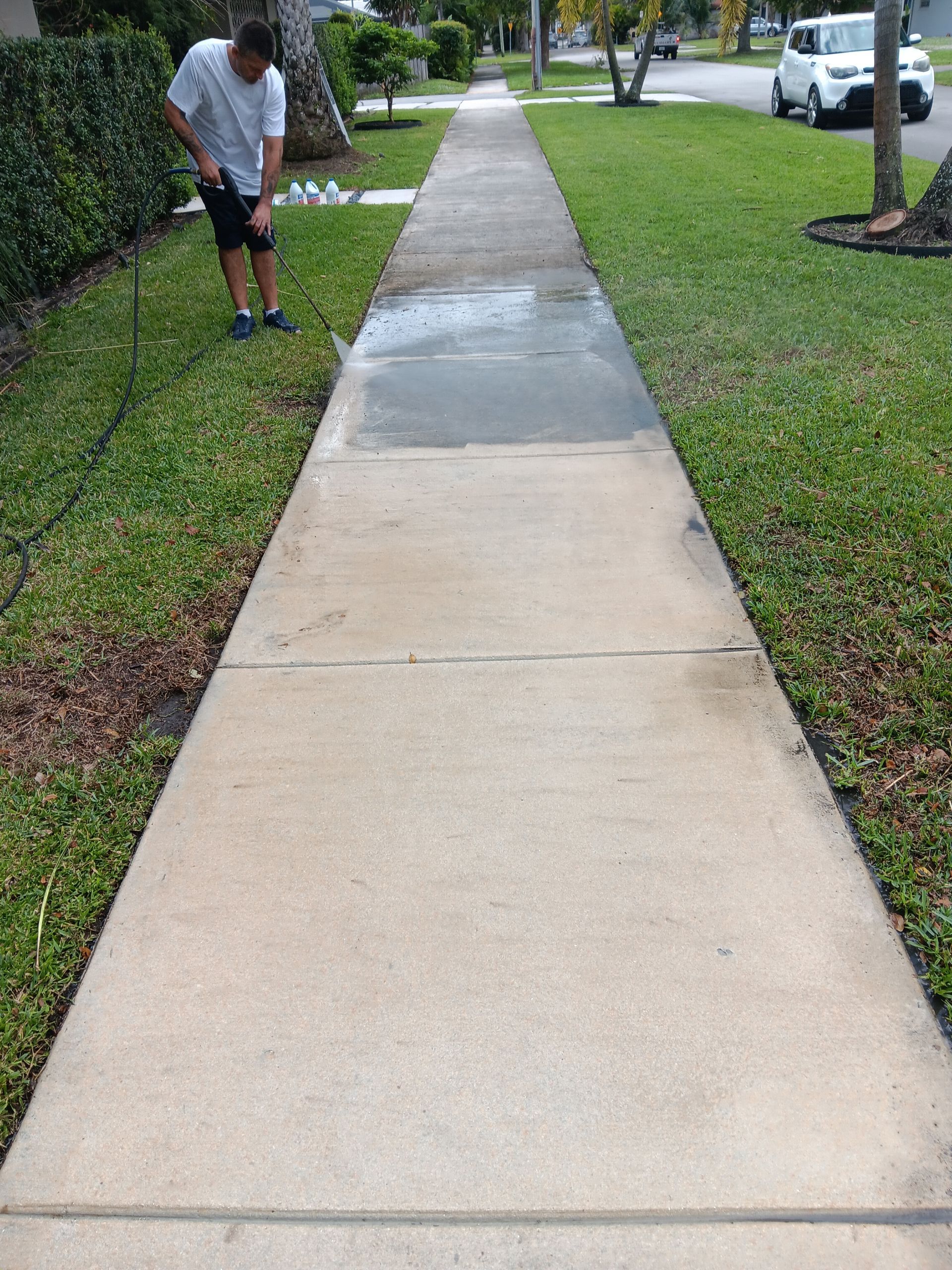Man pressure washing a brick wall and a concrete surface outside a building.