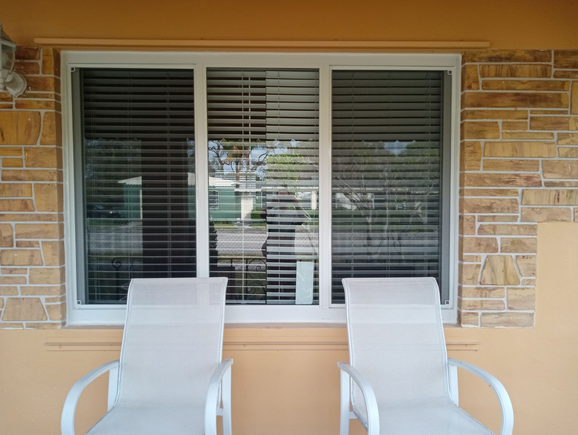 Person in orange hard hat and blue jumpsuit using a drill on a sliding glass door.